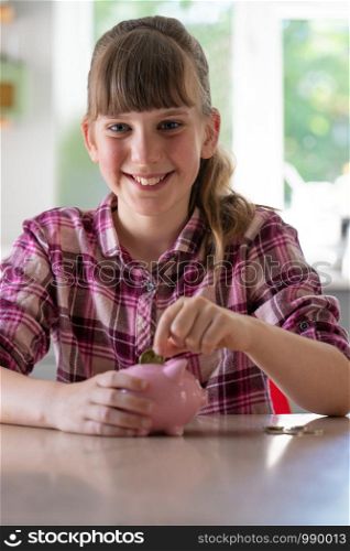 Portrait Of Girl Putting Coins Into Piggybank At Home To Show Saving Money