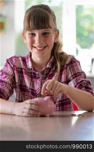 Portrait Of Girl Putting Coins Into Piggybank At Home To Show Saving Money