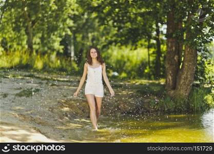 Portrait of girl walking on the water of the lake.. Girl in a white short dress, walks along the waters edge of the pond 6334.