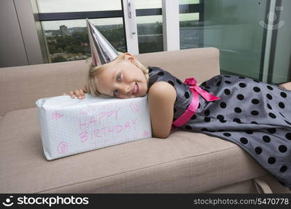 Portrait of girl with birthday gift lying on sofa at home