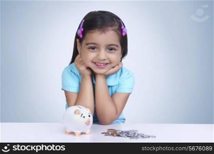 Portrait of girl with coins and piggy bank against blue background