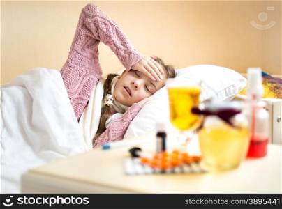 Portrait of girl with high temperature lying in bed and looking on tea with lemon