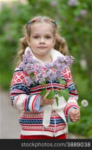 Portrait of girl with lilacs and dandelions in the hands. Half-length portrait four-year girl in a jacket with a bouquet of lilacs and a dandelion in hands