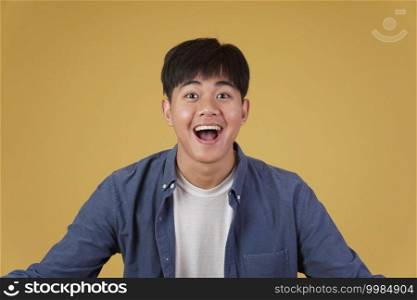 portrait of  glad cheerful happy rejoicing excited overjoyed young asian man dressed casually isolated on yellow studio background