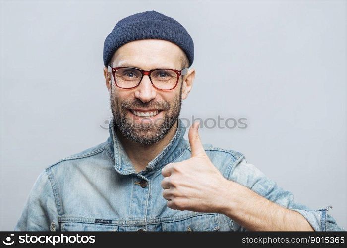 Portrait of glad middle aged male witth thick beard and mustache shows his satisfaction with something, raises thumb, has positive smile on face, isolated over white background. Happiness concept