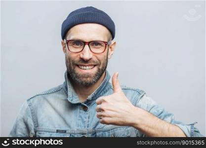 Portrait of glad middle aged male witth thick beard and mustache shows his satisfaction with something, raises thumb, has positive smile on face, isolated over white background. Happiness concept