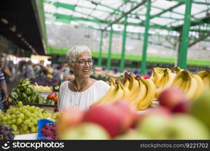 Portrait of good-looking senior woman buys bananas at the market