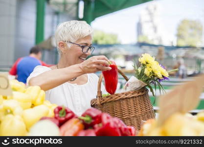 Portrait of good-looking senior woman wearing glasses buys pepper on market