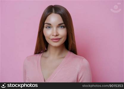 Portrait of good looking young European woman with long hair, has well cared complexion, dressed in casual clothes, isolated over pink background. People, face expressions and beauty concept.