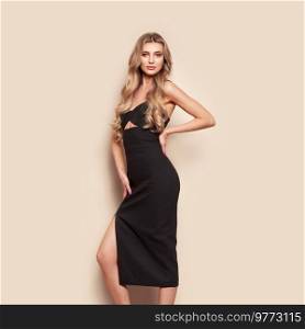 Portrait of gorgeous elegant sensual blonde woman wearing fashion black dress isolated on beige background. Model woman with long curly hairstyle. Care and beauty hair product