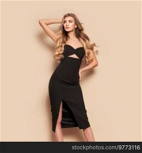 Portrait of gorgeous elegant sensual blonde woman wearing fashion black dress isolated on beige background. Model woman with long curly hairstyle. Care and beauty hair product