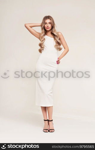 Portrait of gorgeous elegant sensual blonde woman wearing fashion white dress isolated on white background. Model woman with long curly hairstyle. Care and beauty hair product