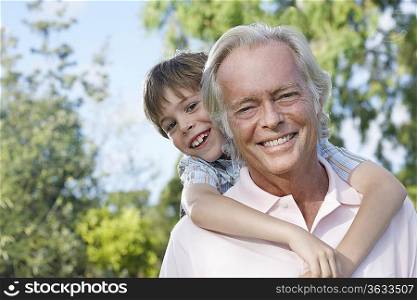 Portrait of grandfather with grandson (7-9) riding piggy back outdoors, smiling