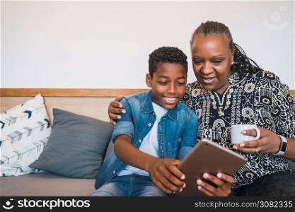 Portrait of grandmother and grandchild taking selfie with digital tablet while sitting on sofa couch at home. Family and lifestyle concept.