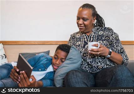 Portrait of grandmother and grandchild using digital tablet while sitting on sofa couch at home. Family and lifestyle concept.