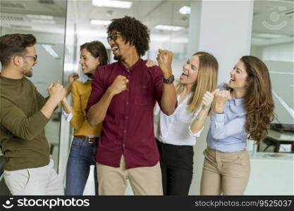 Portrait of group of young excited business people with hands up standing in office
