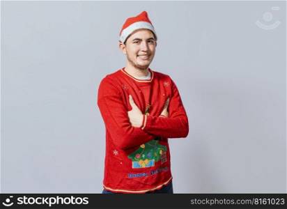 Portrait of guy in sweater and christmas hat with crossed arms isolated. Smiling guy in christmas hat with crossed arms smiling. Teenage guy in christmas clothes with crossed arms smiling