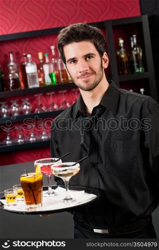 Portrait of handsome barman at bar holding tray with cocktails