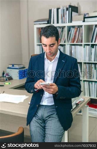 Portrait of handsome businessman looking smartphone sitting over office table. Businessman looking his smartphone in the office