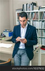 Portrait of handsome businessman looking smartphone sitting over office table. Businessman looking his smartphone in the office