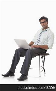 Portrait of handsome businessman on chair using laptop
