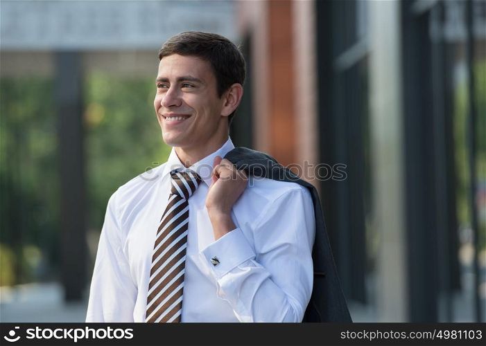 Portrait of handsome businessman standing in front of office building and holding his jacket