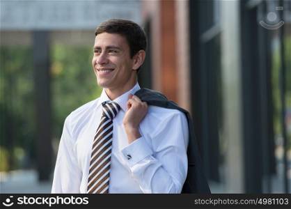 Portrait of handsome businessman standing in front of office building and holding his jacket