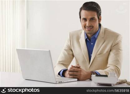 Portrait of handsome businessman with laptop and landline at office desk