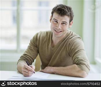 Portrait of handsome businessman writing on document at desk in office