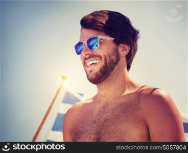 Portrait of handsome cheerful man over blue sky background, traveling on water transport with the Greek flag on board, happy beach holidays