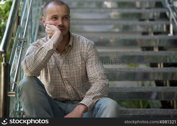 Portrait of handsome confident young businessman sitting on stairs at modern office building
