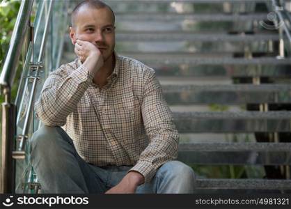 Portrait of handsome confident young businessman sitting on stairs at modern office building