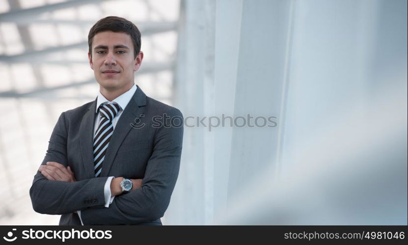 Portrait of handsome confident young businessman standing arms crossed, looking at camera.