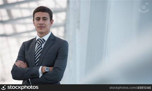 Portrait of handsome confident young businessman standing arms crossed, looking at camera.