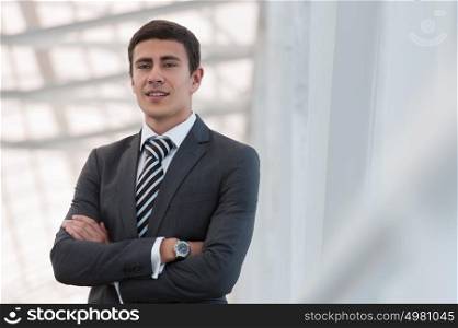 Portrait of handsome confident young businessman standing arms crossed, smiling happy, looking at camera.