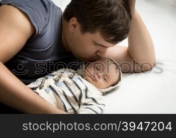 Portrait of handsome daddy kissing baby boy lying on bed