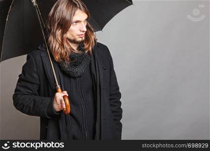Portrait of handsome fashionable man wearing black coat and scarf holding umbrella. Young guy posing in studio. Winter or autumn fashion.. Handsome fashion man portrait wearing black coat.