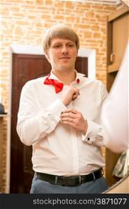 Portrait of handsome groom putting on white shirt at home