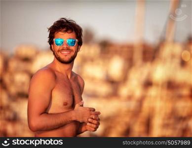 Portrait of handsome guy on the beach in mild yellow sunset light, perfect athletic body, summer vacation on luxury sailboat
