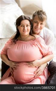 Portrait of handsome man hugging chubby pregnant wife from back