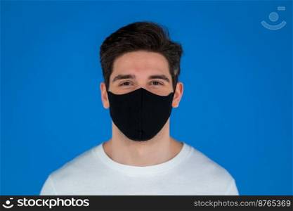 Portrait of handsome man in facial medical mask looking to camera. Guy in studio on blue background. Covid-19, coronavirus, new reality concept. High quality photo. Portrait of handsome man in facial medical mask looking to camera. Guy in studio on blue background. Covid-19, coronavirus, new reality concept.
