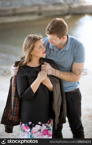 Portrait of handsome man putting jacket on girlfriends shoulders at riverbank