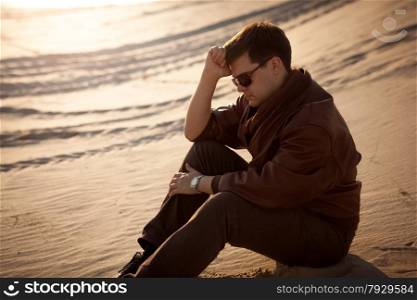 Portrait of handsome man sitting and thinking on sand dune