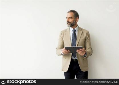 Portrait of handsome senior businessman with digital tablet by the white wall