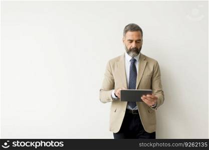 Portrait of handsome senior businessman with digital tablet by the white wall