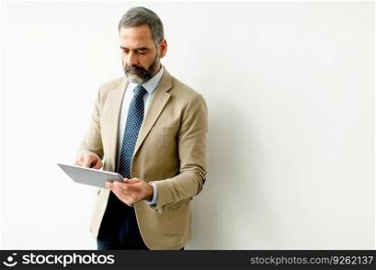 Portrait of handsome senior businessman with tablet by wall