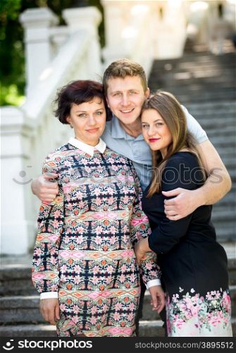 Portrait of handsome smiling man hugging mother and girlfriend at park