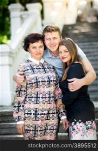 Portrait of handsome smiling man hugging mother and girlfriend at park