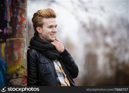 Portrait of handsome smiling man outdoor in city setting, male model wearing winter clothes black jacket and scarf against colorful graffiti wall
