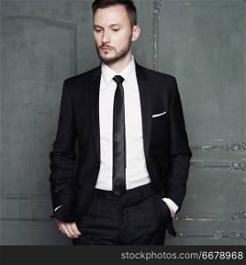 Portrait of handsome stylish man in elegant black suit. Sexy young man in stylish smoking pose in dark studio. Glamour photography of  fashionable male model.